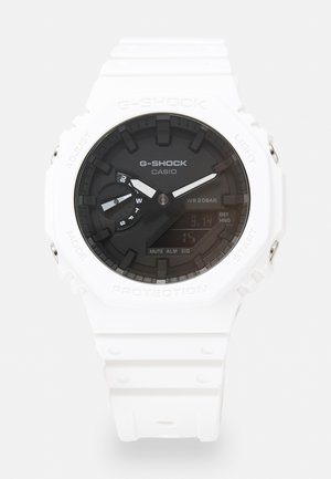Weiße G-Shock-Uhr mit schwarzem Zifferblatt, analogen und digitalen Anzeigen, strukturiertem Kunststoffgehäuse und Gummiband. Wasserdicht bis 20 bar.