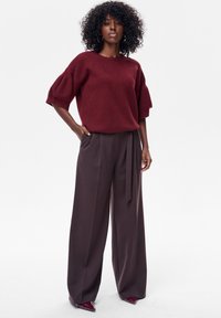 Bordowy, dziergany sweter z krótkimi, bufkowatymi rękawami, zestawiony z luźnymi, wysokim stanem, ciemnobrązowymi spodniami z wiązanym paskiem w talii.