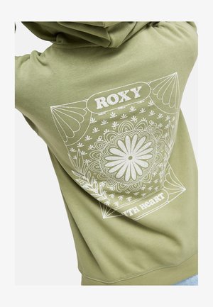 Person wearing an olive green sweatshirt with a large white floral mandala and "ROXY" text printed on the back.