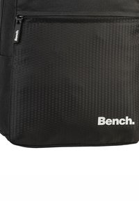Zwarte rugzak met honingraatpatroon, voorzien van een ritszak aan de voorkant en een wit "Bench." logo rechtsonder.