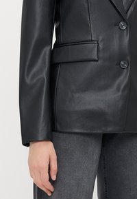 Černý kožený blazer s klopami, dvěma předními knoflíky a boční kapsou. Vyznačuje se hladkou texturou a strukturovaným střihem.