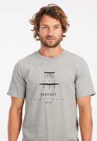 Grijze katoenen T-shirt met een zwart grafisch ontwerp van een skateboard en surfplank, met de tekst "PROTEST SPORTSWEAR EST. 93" eronder.