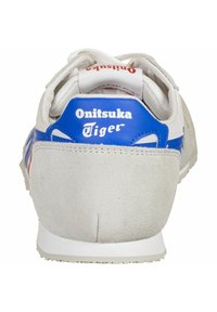 Hvide sneakers med blå accenter og grå ruskind hæl. Har en rund form og en kontrasterende rød logo på hælklappen. Tekstureret sål.