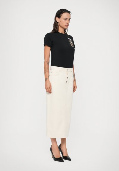 Camiseta negra con un diseño gráfico, combinada con una falda de mezclilla blanca a la altura de la rodilla que cuenta con un cierre de botones y cinco bolsillos. Tacones altos negros.
