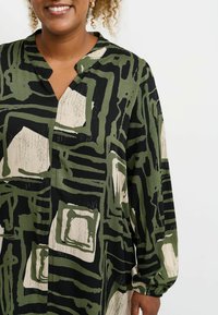 Dlhý rukáv košele v čiernej a olivovej zelenej farbe s abstraktnými vzormi. Obsahuje klopaný golier a rad gombíkov, vyrobená z ľahkého materiálu.