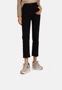 Jeans cropped neri con orli sfrangiati, abbinati a sneakers color sabbia chiaro realizzate in materiale mesh e suede, con una suola a cuneo stratificata.