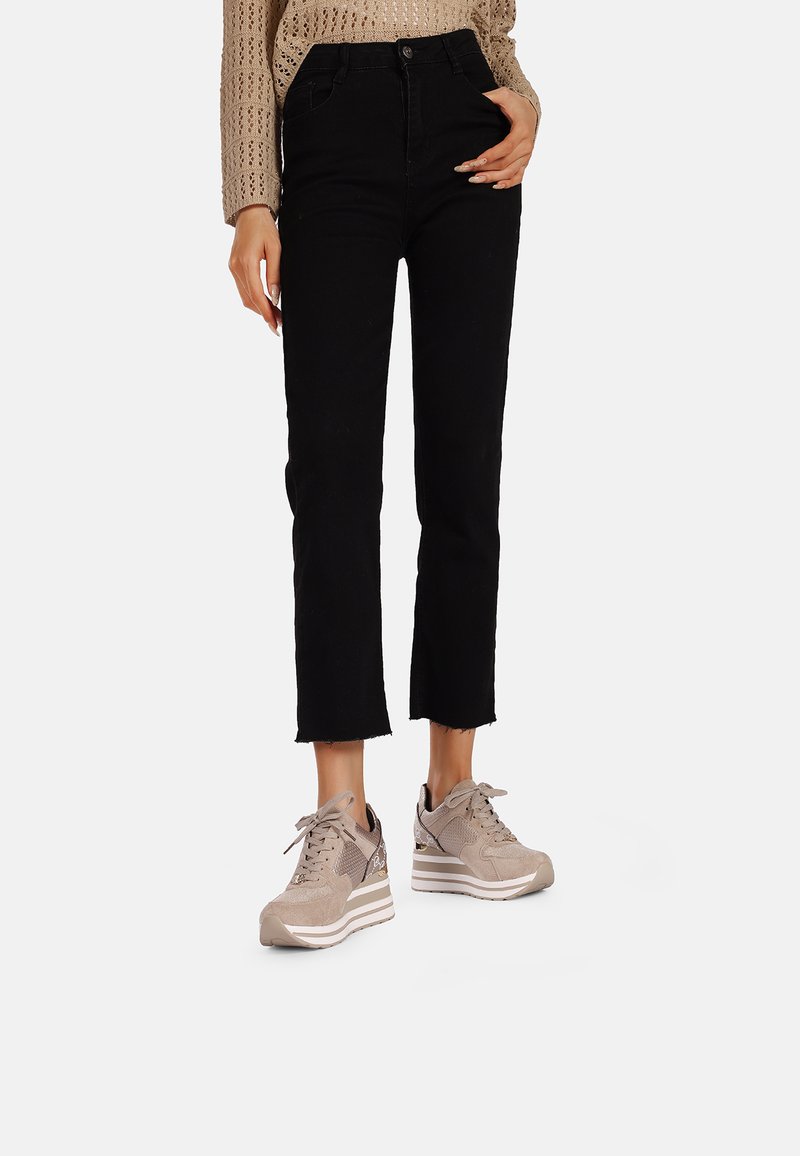 Jeans cropped neri con orli sfrangiati, abbinati a sneakers color sabbia chiaro realizzate in materiale mesh e suede, con una suola a cuneo stratificata.