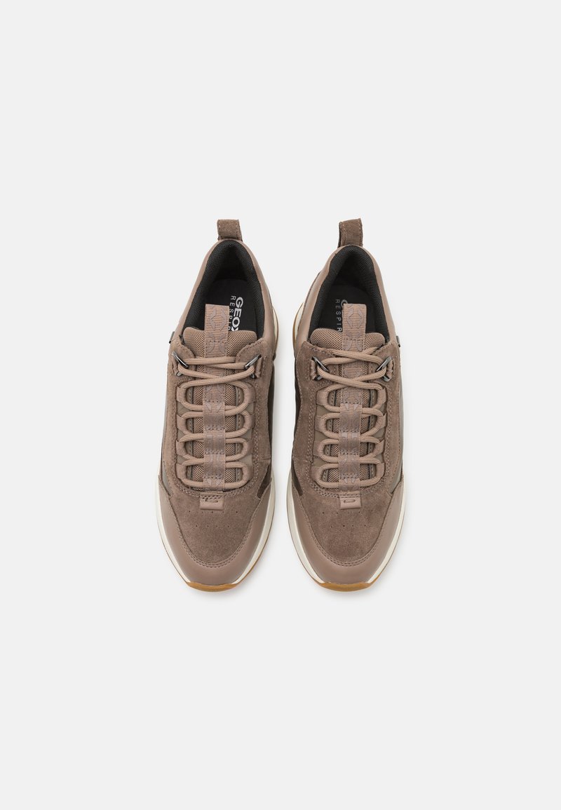 Sneaker in suede marrone con accenti testurizzati e lacci elastici. Presenta una suola intermedia bianca e una suola in gomma color caramello. Vista dall'alto.