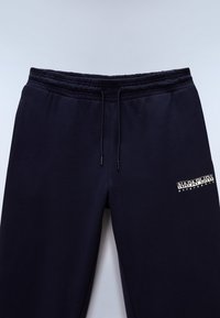 Granatowe spodnie dresowe z elastycznym pasem i sznurkami, z białym logo "Napapijri geographic" na górnej części uda.