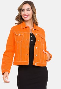 Orangene Jeansjacke mit weißen Nähten, klassischem Kragen, Druckknopfverschluss und zwei Brusttaschen. Über einem schwarzen Kleid getragen.