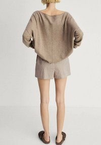 Beige oversized trui met een wijde halslijn, zachte textuur en lange mouwen, gecombineerd met lichtgestreepte shorts en bruine instappers.
