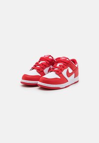 Raudoni ir balti Nike sportbačiai, pagaminti iš odos, su perforuota pirštų vieta, apvaliais raišteliais ir išraiškingu Nike logotipu šone.