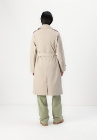 Beige trenchcoat med belte i midjen, lange ermer og rett snitt. Har en ventil bak for bedre bevegelsesfrihet.