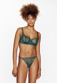 Set di lingerie in rete verde con reggiseno a spalline larghe e ferretto, e perizoma abbinato con sottili fasce laterali, entrambi con rifiniture a contrasto.