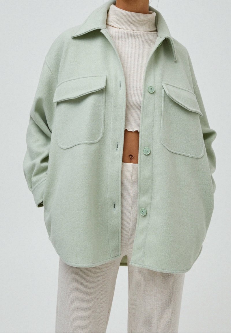 Shacket oversize verde chiaro realizzato in tessuto morbido, con due tasche sul petto, chiusura frontale con bottoni e colletto appuntito.