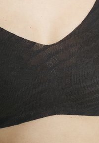 Black bra featuring a textured, wavy pattern with a plunging neckline. Material appears lightweight and stretchy, designed for comfort.