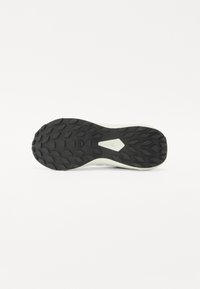 Semelle extérieure en caoutchouc noir avec des motifs de texture et des crampons de traction ; semelle intermédiaire de couleur claire avec une finition lisse ; design épuré.