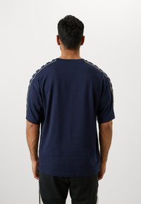 T-shirt à manches courtes bleu marine, avec des rayures contrastées le long des épaules et une coupe décontractée. Matière en coton doux sans logos visibles.
