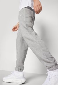 Grijze joggings broek met taps toelopende enkels, elastische tailleband en zijzakken, gecombineerd met witte sportschoenen. Zachte, gestructureerde stof.