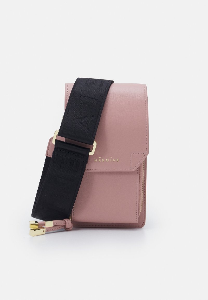 Růžová kožená crossbody taška s černým popruhem, zdobená raženým písmem. Zlaté kovové doplňky a detaily s kapsou na zip. Kompaktní obdélníkový tvar.