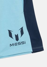 Camisa atlética azul claro com detalhes em azul escuro, um padrão texturizado e um logotipo preto com o nome "MESSI" impresso abaixo.