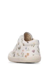 Vit liten barnsko med blommönster och insektstryck, med två kardborreband och en texturerad gummisula, visad från baksidan.