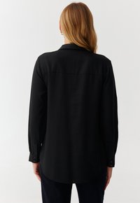 Black long-sleeve shirt with a buttoned cuff, a pointed collar, and a rounded hem, made from a smooth, lightweight fabric.
