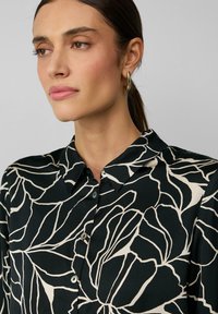 Zwarte blouse met een kraag, voorzien van een ivoren bloemenpatroon, knoopsluiting en een gladde zijdeachtige textuur.