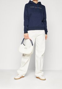 Sudadera de marina con logo blanco, pantalones de pierna ancha color crema, zapatillas blancas y un bolso color crema con asas rosas y marinas.