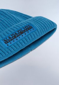 Blå stickad mössa med ribbad textur och en vikt uppkant som visar en rektangulär svart och blå etikett med texten "NAPAPIJRI".