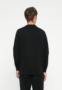 Black sweatshirt with long sleeves and a crew neck. Features ribbed cuffs and hem, smooth texture, minimalistic design without patterns.