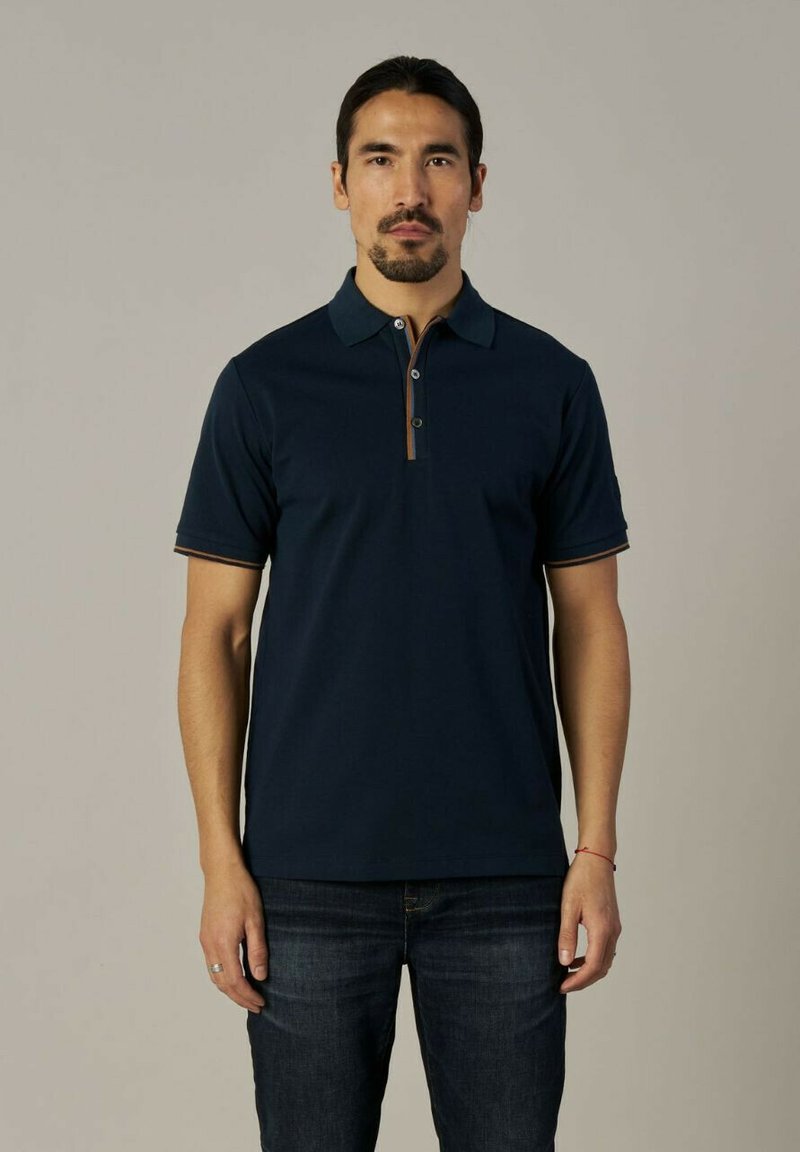 Tumesinine polosärk krae, lühikeste varrukatega ja kahe nööbiga nööpide rida. Omab kontrastset õmblust ja pehmet tekstuuri. Kombineeritud tumedate teksadega.