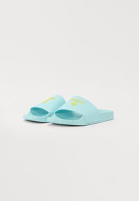 Lyseblå sklisikre sandaler i gummi. Har en bred stropp med gul "GUESS"-merkevare og et enkelt, flatt design.