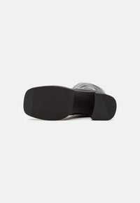 Semelle de chaussure en caoutchouc noir avec une surface texturée et un léger talon, présentant un bord supérieur lisse pour plus de durabilité.