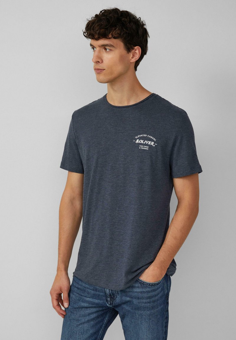 Donkergrijze katoenen t-shirt met korte mouwen, ronde halslijn en een kleine witte print op de borst. Draagt met blauwe denim jeans.