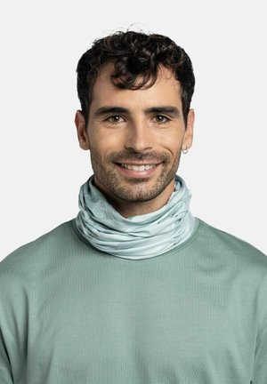 Man with short curly dark hair, light beard, wearing a light blue neck gaiter and green shirt, smiling against a plain background.