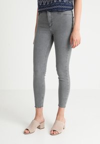 Jeans skinny grises de cintura alta, con dobladillo deshilachado. Combinados con mule de tacón abierto en color beige. El material parece de tipo denim.