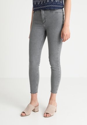 Jeans skinny grises de cintura alta, con dobladillo deshilachado. Combinados con mule de tacón abierto en color beige. El material parece de tipo denim.