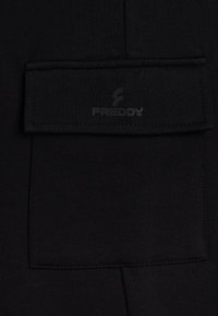 Pantaloni sportivi neri con tasca a toppa, texture morbida e dettagli cuciti. Logo stampato sulla tasca per il branding.