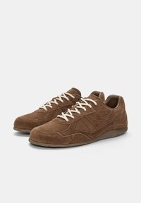 Sneaker in suede marrone con design a profilo basso, lacci bianchi, superficie texture e accenti sottili sui lati. Suola in gomma.