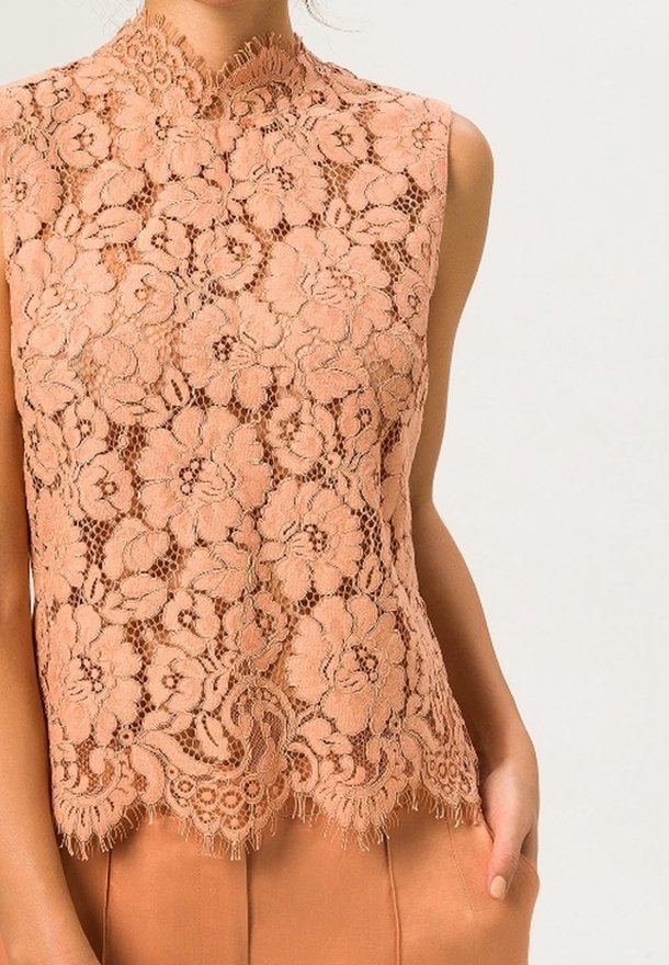 Ferskenfarvet blonde top med høj hals, blomsterprint og bølget kant. Gennemsigtig tekstur med en tætsiddende silhuet.