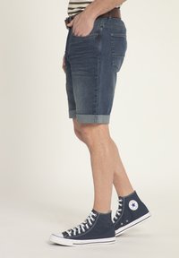 Pantaloni corti in denim di colore blu scuro con orlo arrotolato, abbinati a sneaker alte blu navy con accenti e lacci bianchi.