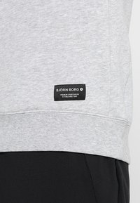 Szara bluza z miękkiego materiału, z zaokrąglonym dołem i czarną metką z białym napisem: "BJÖRN BORG PREMIUM SPORTSWEAR ESTABLISHED 1984."