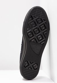 Semelle d'une Converse All Star noire avec motif texturé et logo de la marque sur un fond blanc en angle.