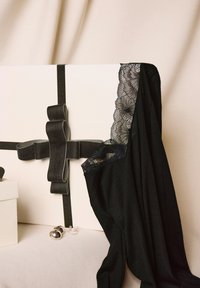 Zwarte kleding met kantdetails, zorgvuldig over een crème cadeau-doos gedrapeerd, met een zwarte satijnen strik en zilveren oorbellen ernaast, op een beige ondergrond.