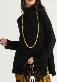Pull noir en tricot avec col roulé, bords côtelés, manches larges et fentes latérales, associé à un collier multicolore en perles et un pantalon à motifs.