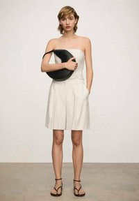 Strapless cream top with vertical stripes, matching high-waisted shorts, and black bag with circular shape; flat black sandals complete the look.
