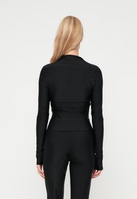 Blusa preta de mangas compridas com um design justo, textura suave e mangas até o pulso, combinada com leggings pretas a condizer.