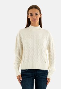 Maglione lavorato a maglia a trecce color crema con colletto e orlo a coste, caratterizzato da una vestibilità ampia e maniche lunghe. Accentuato da un piccolo logo.