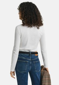 Witte lange mouwen shirt in combinatie met blauwe spijkerbroek. Het shirt heeft een gladde textuur. De spijkerbroek heeft een donkere tailleband en achterzakken.